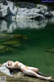 A woman in an orange bikini laying on a rock in the water.